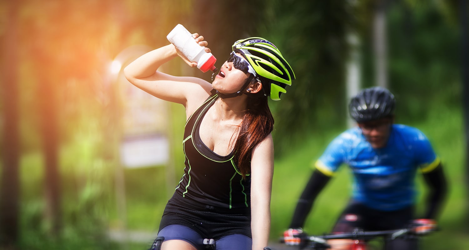 Ciclista donna che beve acqua mentre va in bicicletta perché fa caldo