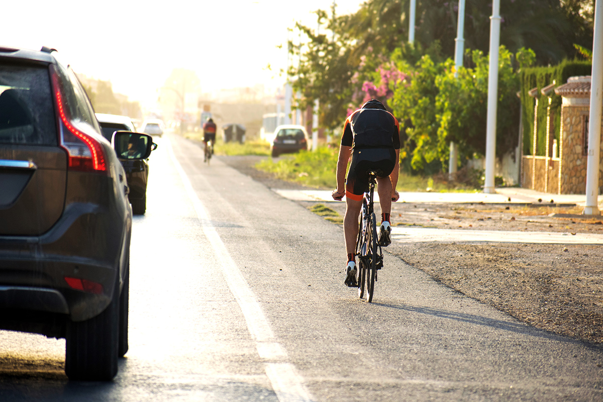 Ciclista pedala su strada lungo le auto che passano accanto a lui mantenendo la distanza di sicurezza