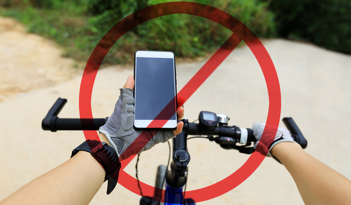 Il ciclista usa lo smartphone quando va in mountain bike su un sentiero e simbolo di divieto sopra la foro 